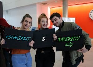 3 students holding boards reading #STANDOUT and Progress